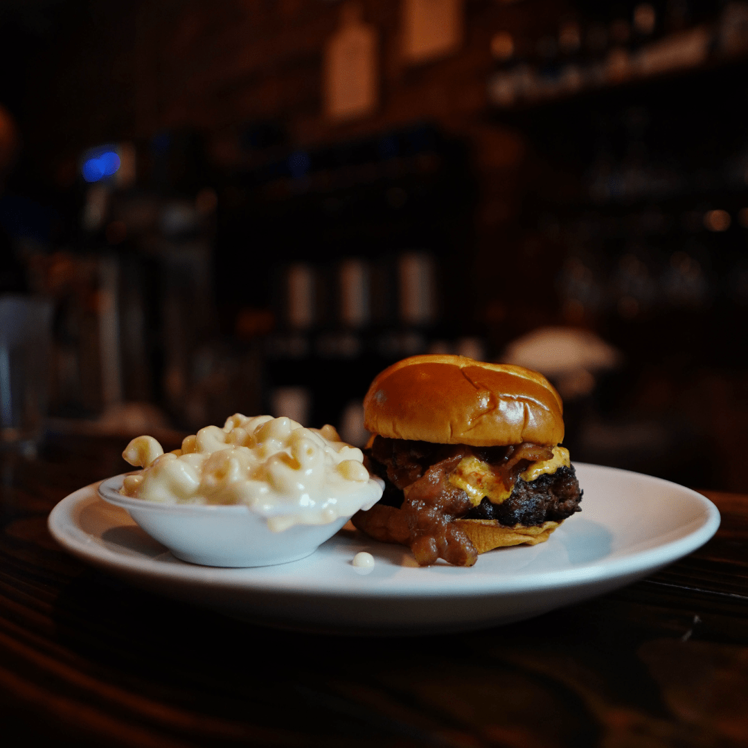 A delicious bacon burger served with creamy mac and cheese on a plate, ready to be enjoyed