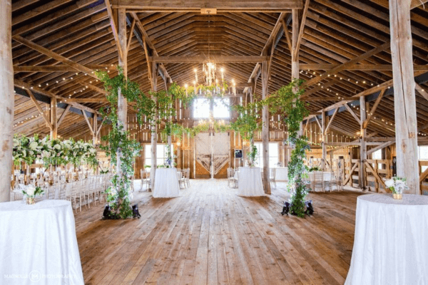 A beautifully decorated rustic barn wedding venue at The Barn at May-Lew Farm in Greenville, NC, with chandeliers and greenery.