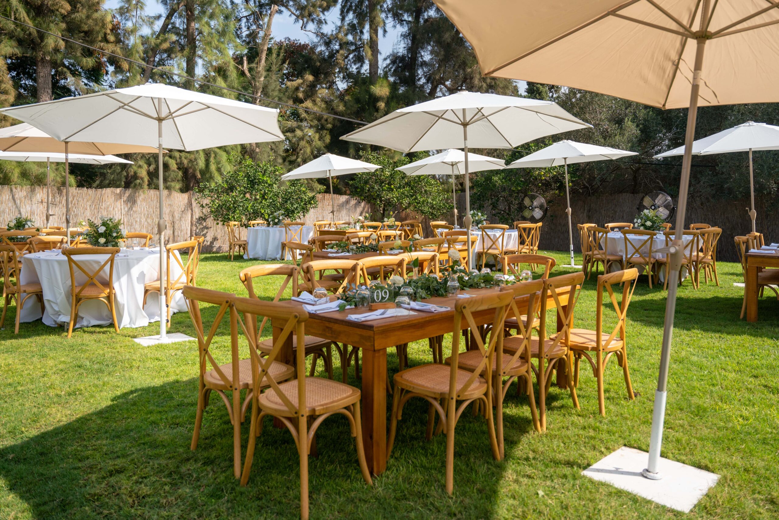 Tables set under white parasols, decorated with delicate bouquets, prepared for a wedding ceremony.